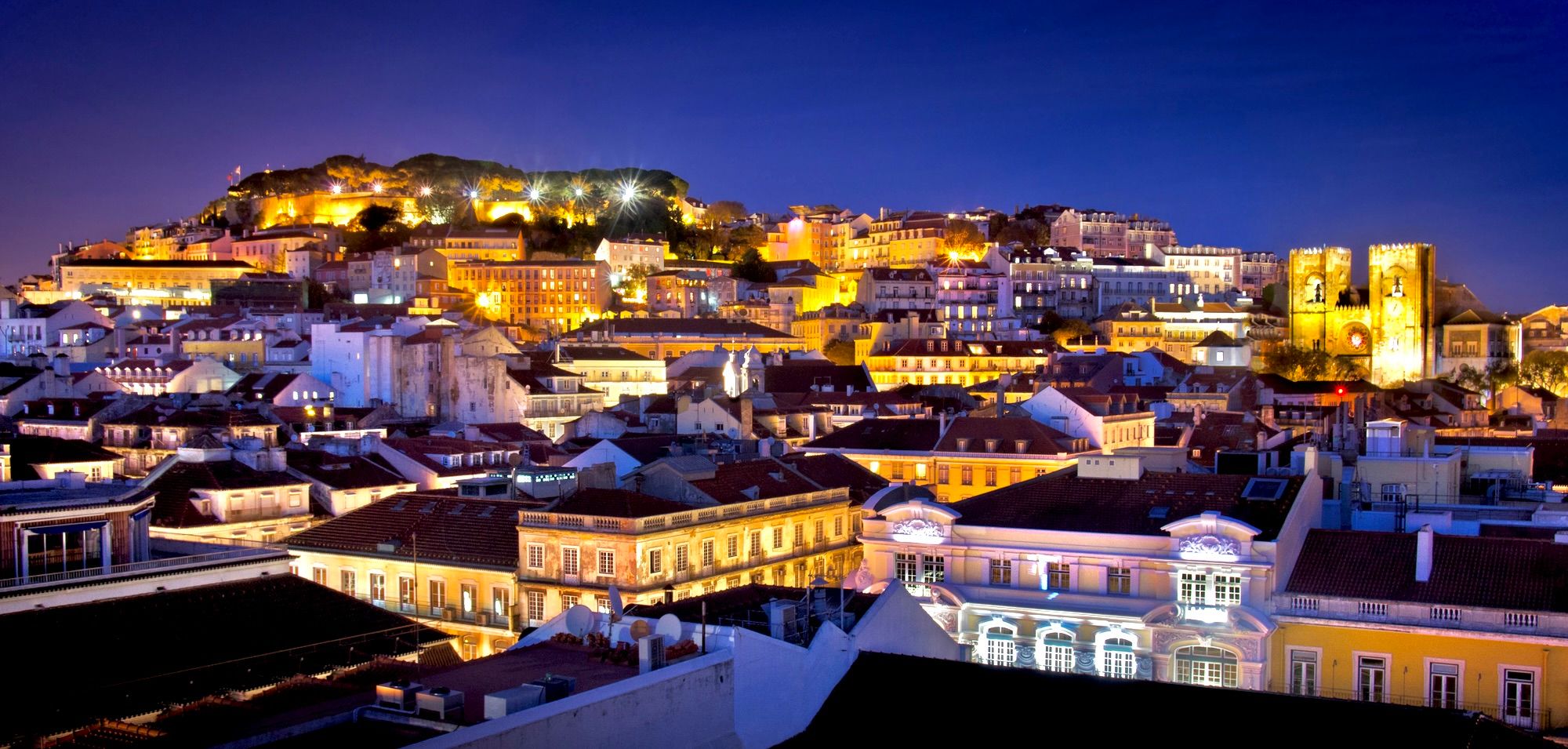 Lisbon at twilight — São Jorge Castle and the Sé cathedral lit over the rooftops of the old city